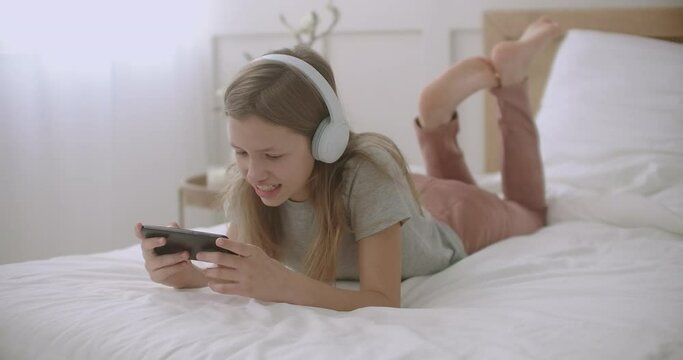 school girl is using app in smartphone, lying in bedroom and talking, leisure of children in weekend