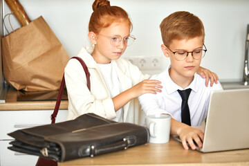 Obraz premium adorable redhead child girl supports boyfriend boy working on laptop, she is listening to his problems at work, deadlines. at home