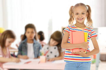 Happy little girl with notebooks in classroom