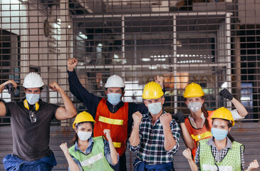 Happy group of industrial worker wearing protective face mask celebrating after factory reopen at...