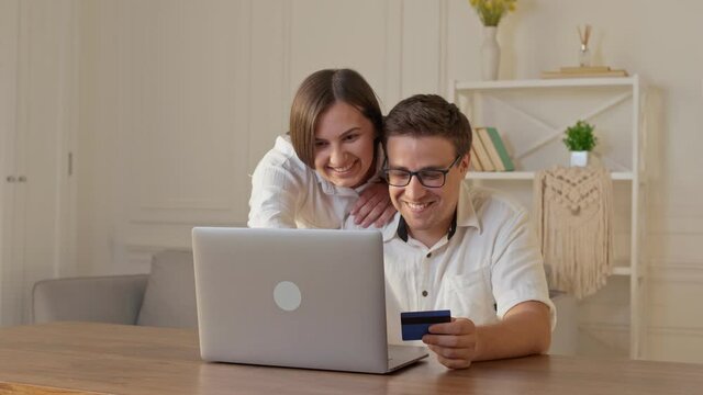Cheerful Young Couple Shopping Online While Sitting Home With Credit Card and Laptop Computer. Mutual family's purchases. Purchase Confirmation by the Internet. Binding a Card for Online Shopping