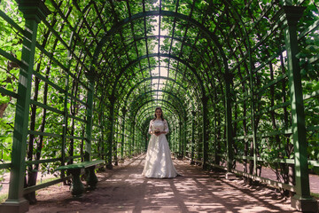 Plakat Bride with wedding bouquet in hands on background of green leaves in the Park. Pretty woman in wedding dresses on Sunny wedding day. Female in amazing view. Happy bride on background green