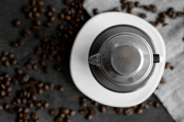 White cup of coffee with a metal filter on a top and scattered beans on a wooden table. Traditional vietnamese coffee.