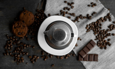 White cup of coffee with a metal filter on a top and scattered beans on a wooden table. Traditional vietnamese coffee.