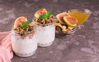 
Two jars with fig yogurt, berries and honey on a gray background.