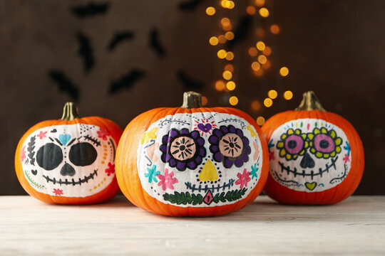 Pumpkins with catrina skull makeup on brown background with blurred lights