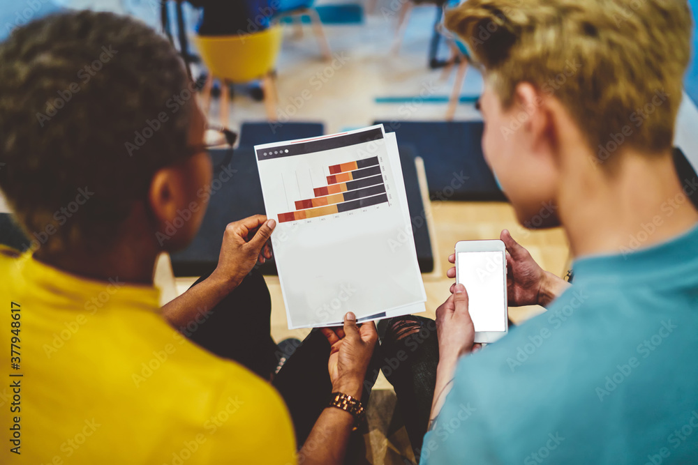 Poster back view of millennial startupers analyzing financial documents with graph charts checking informat