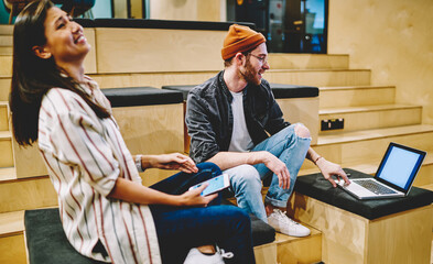 Happy multiracial male and female hipsters having fun together on break watching videos on laptop...