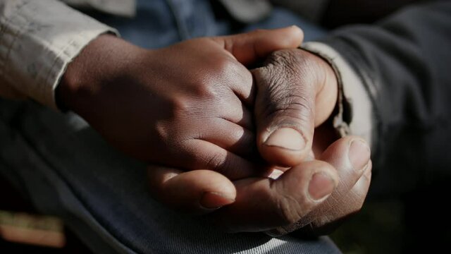 A man is clasping a boy's hand in his outside during the day
