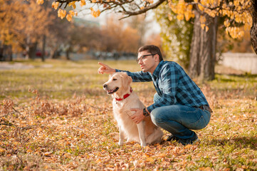 Fototapeta premium Portrait of young man sitting hugging with golden retriever dog. Friendship, pet and human. Man playing with dog