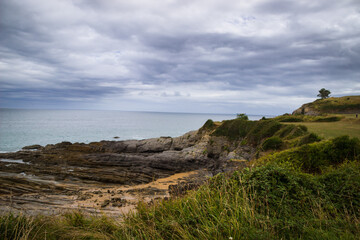 Imagen de playa acantilado con cielo nublado rocas y zonas verdes en cantabria
