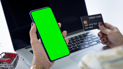 A picture of a beautiful woman shopping online with a credit card and a phone in a green screen with a laptop on the table.