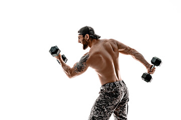 Muscular athlete bodybuilder man in camouflage pants with a naked torso punching with dumbbells like boxer on a white background.