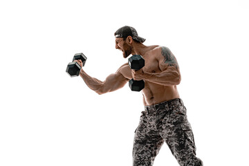 Muscular athlete bodybuilder man in camouflage pants with a naked torso punching with dumbbells...