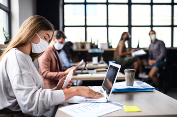 People with face masks disinfecting indoors in office, back to work after coronavirus lockdown.