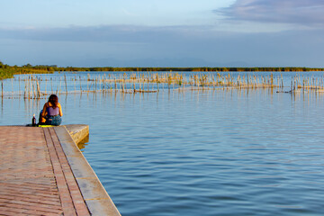Fototapeta na wymiar On a pier, woman sitting on her back
