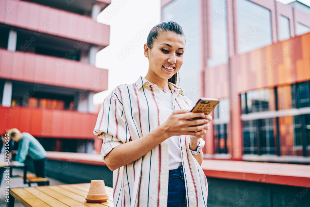 Poster cheerful japanese hipster blogger reading received notification in social networks using modern smar