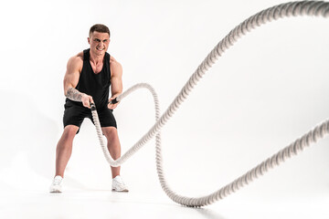 Attractive muscular man working out with heavy ropes. Photo of handsome man in sportswear isolated on white background. Crossfit
