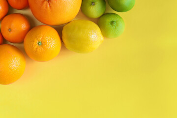 Citruses are laid out in gradient composition in upper left corner of background. Tangerines, oranges, grapefruits, lemons, limes are lying on yellow canvas. Summer exotic tropical fruits.
