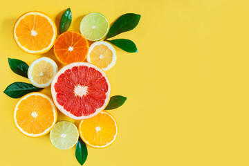 Slices of citruses are laid out in composition in left side of background. Pieces of tangerines, oranges, grapefruits, lemons, limes are lying on yellow canvas. Summer exotic tropical fruits.