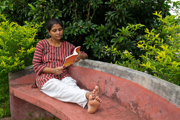 A beautiful woman in casual clothing, sitting on a red bench is reading a book and thinking about the story in a park 