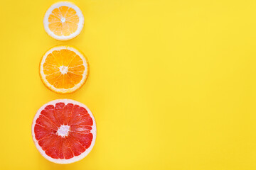 Slices of citruses are laid out in gradient composition in left side of background. Pieces of orange, grapefruit, lemon are lying on yellow canvas. Summer exotic tropical fruits  concept.