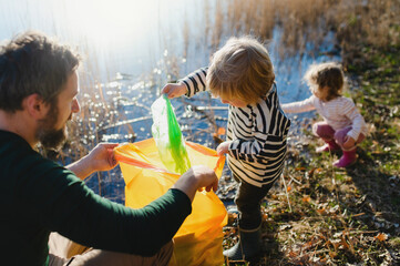 Father with small kids collecting rubbish outdoors in nature, plogging concept.