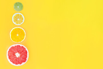 Slices of citruses are laid out in gradient composition in left side of background. Pieces of orange, grapefruit, lemon, lime are lying on yellow canvas. Summer exotic tropical fruits concept.