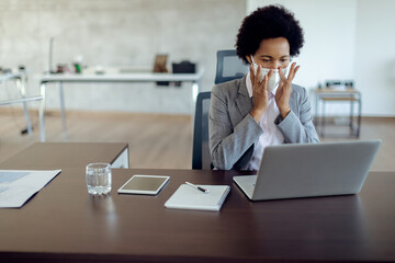 African American businesswoman adjusting face mask while working on laptop in the office.