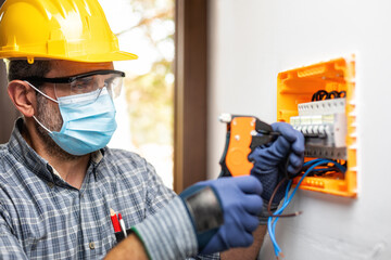 Electrician at work with face protected by surgical mask to prevent Coronavirus infection. Covid-19 pandemic.