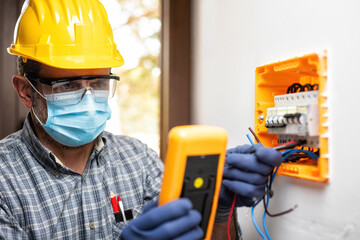 Electrician at work with face protected by surgical mask to prevent Coronavirus infection. Covid-19...