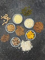 Various grains in glass gravy boats on a black actual stone surface.