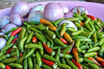 Green chillies, small red chillies and red onions on a white plate. Most of the food components rich in this herb are local food of Thai people.