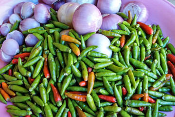 Green chillies, small red chillies and red onions on a white plate. Most of the food components rich in this herb are local food of Thai people.