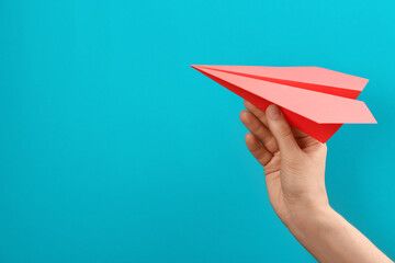 Woman holding paper plane on light blue background, closeup. Space for text