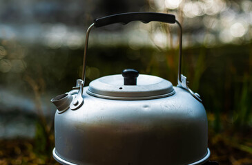 A simple steel kettle boiling water by the waters edge on a hike.