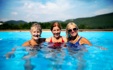 Front view of cheerful senior women in swimming pool outdoors in backyard.