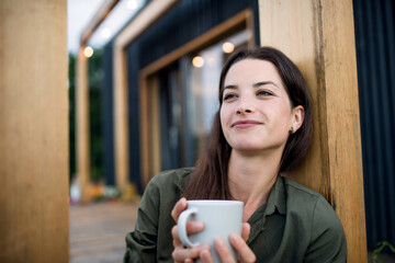 Young woman with coffee outdoors, weekend away in container house in countryside.