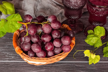 a bunch of pink grapes in a wicker basket and wine glasses on a wooden background close-up. background with grapes and wine in purple glasses