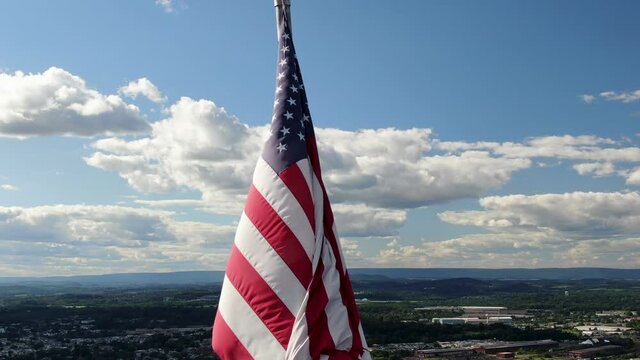 American flag close-up aerial, USA pride, Old Glory waves in wind on sunny summer day, urban city town center in valley below in distance, pulll-back reveals wide panorama