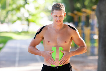 Portrait of handsome young caucasian professional bodybuilder with elastic kinesiology tapes on...