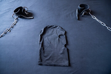 Role-play mask and leather handcuffs on a black sheet. BDSM equipment.