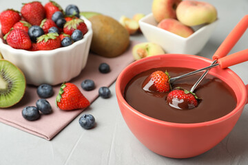 Fondue pot with chocolate and different products on grey table