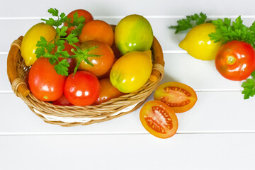 fresh ripe red tomatoes in a wicker basket on a white background. basket of ripe tomatoes on the table. tomatoes and sprigs of parsley close-up.