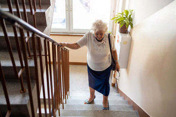 Senior woman climbing staircase with difficulty 
 - Powered by Adobe