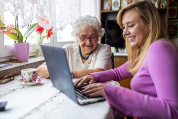 Adult granddaughter teaching her elderly grandmother to use laptop
