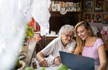 Adult granddaughter teaching her elderly grandmother to use laptop
