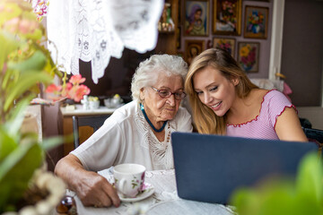 Adult granddaughter teaching her elderly grandmother to use laptop
