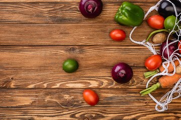 top view of fresh ripe vegetables scattered from string bag on wooden table