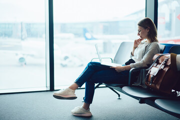 Smiling female traveler browsing laptop in airport terminal